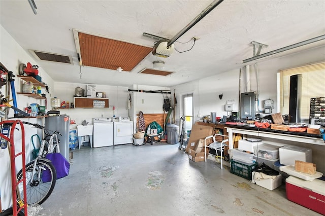 garage featuring a garage door opener, sink, washer and dryer, electric panel, and a workshop area