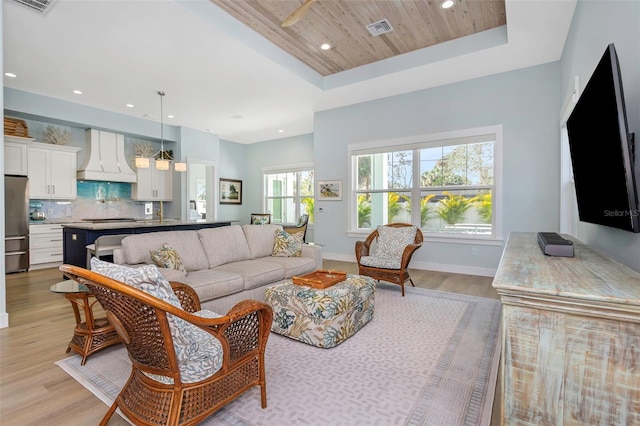 living room with ceiling fan, wooden ceiling, light hardwood / wood-style floors, and a tray ceiling