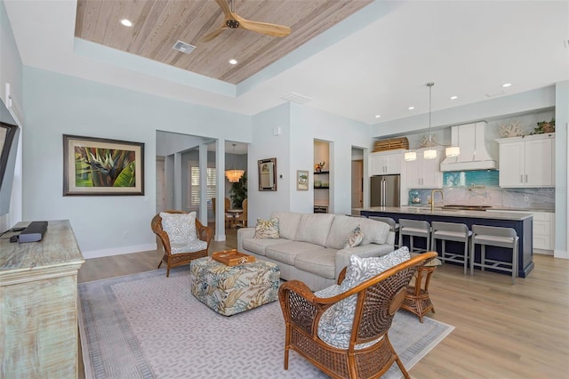 living room with sink, wood ceiling, a raised ceiling, ceiling fan, and light hardwood / wood-style floors