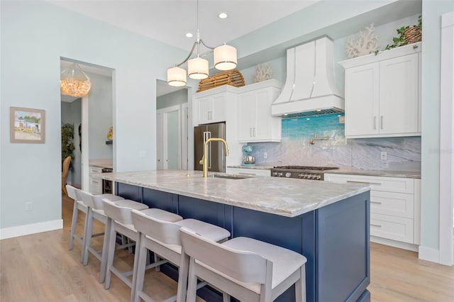 kitchen with custom exhaust hood, white cabinetry, pendant lighting, and a center island with sink