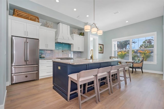 kitchen featuring a kitchen island with sink, hanging light fixtures, white cabinets, custom exhaust hood, and high end refrigerator