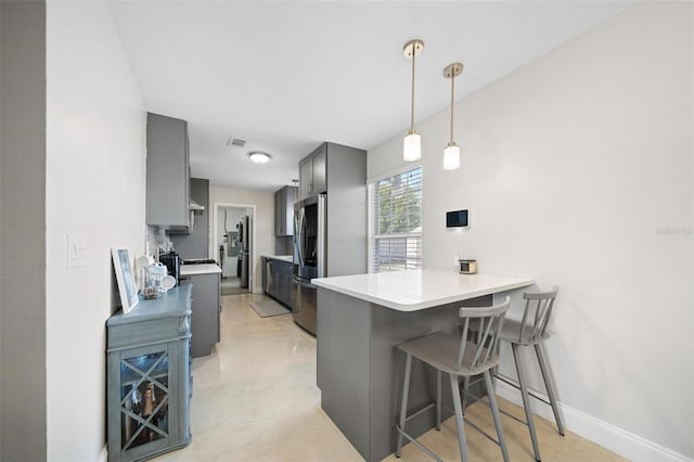 kitchen featuring stainless steel refrigerator, gray cabinetry, a kitchen breakfast bar, stove, and kitchen peninsula