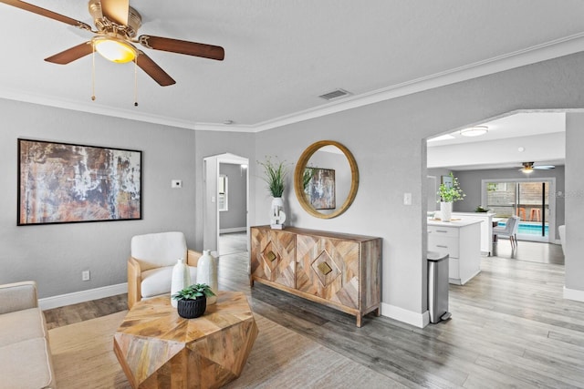 living area with light wood finished floors, visible vents, ornamental molding, ceiling fan, and baseboards