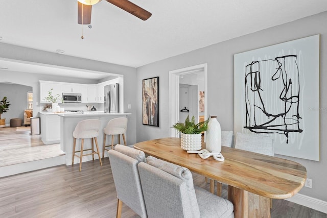 dining room with light wood-type flooring, a ceiling fan, and baseboards