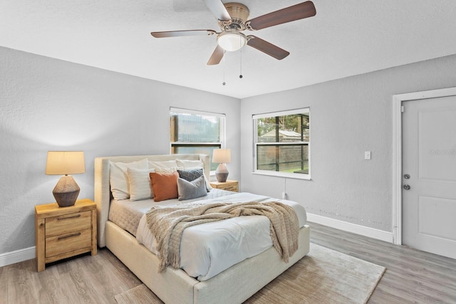 bedroom featuring a ceiling fan, a textured wall, light wood-style flooring, and baseboards