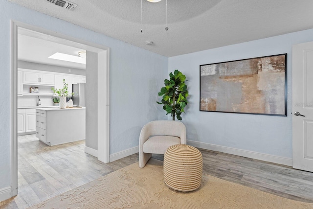 sitting room with a textured ceiling, a skylight, visible vents, baseboards, and light wood-type flooring