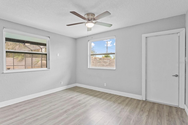 empty room with a ceiling fan, baseboards, a textured ceiling, and light wood finished floors