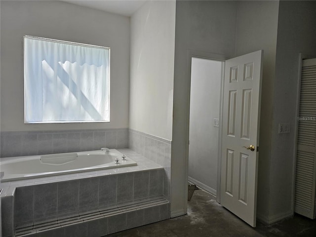 bathroom featuring a relaxing tiled tub and concrete flooring