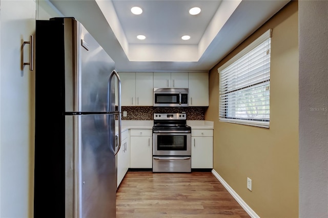 kitchen with light hardwood / wood-style flooring, stainless steel appliances, tasteful backsplash, white cabinets, and a raised ceiling