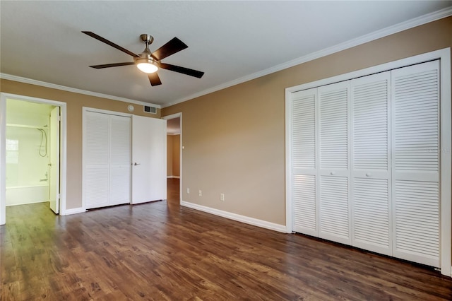 unfurnished bedroom with dark wood-type flooring, connected bathroom, crown molding, multiple closets, and ceiling fan