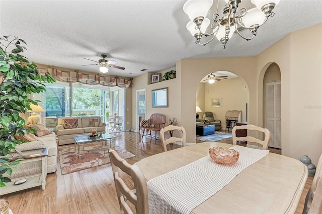 dining space with ceiling fan with notable chandelier, light hardwood / wood-style flooring, and a textured ceiling