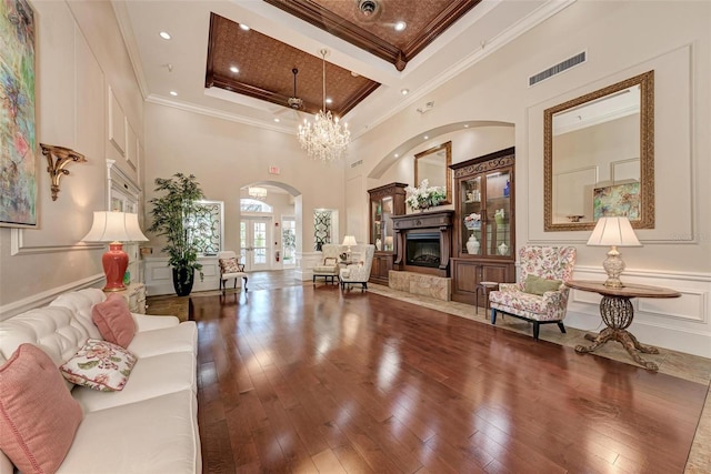 living room featuring hardwood / wood-style flooring, ornamental molding, a chandelier, and a towering ceiling