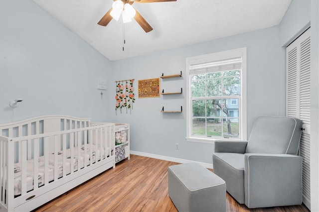 bedroom featuring a nursery area, hardwood / wood-style floors, ceiling fan, and a closet