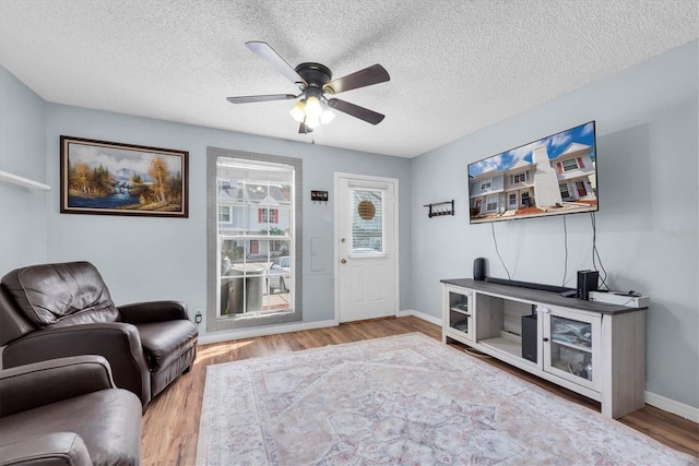 living area with ceiling fan, a textured ceiling, wood finished floors, and baseboards