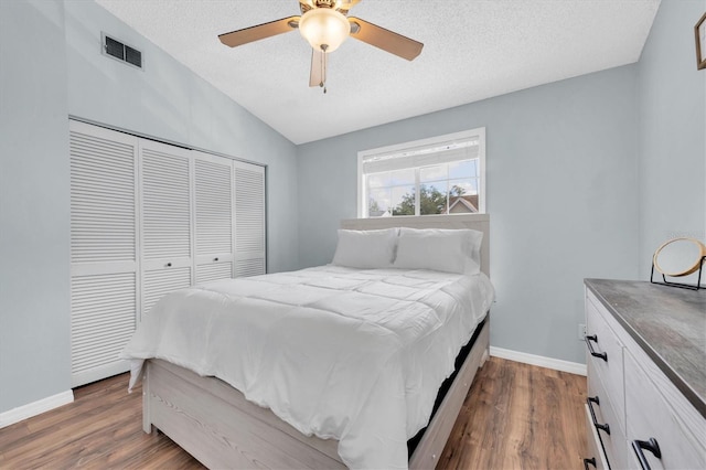 bedroom with dark wood-type flooring, vaulted ceiling, a closet, and a textured ceiling