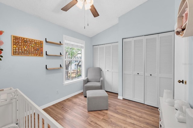 bedroom featuring vaulted ceiling, two closets, light wood-type flooring, ceiling fan, and a textured ceiling