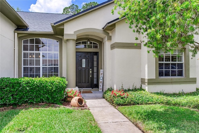 view of exterior entry featuring stucco siding and a shingled roof