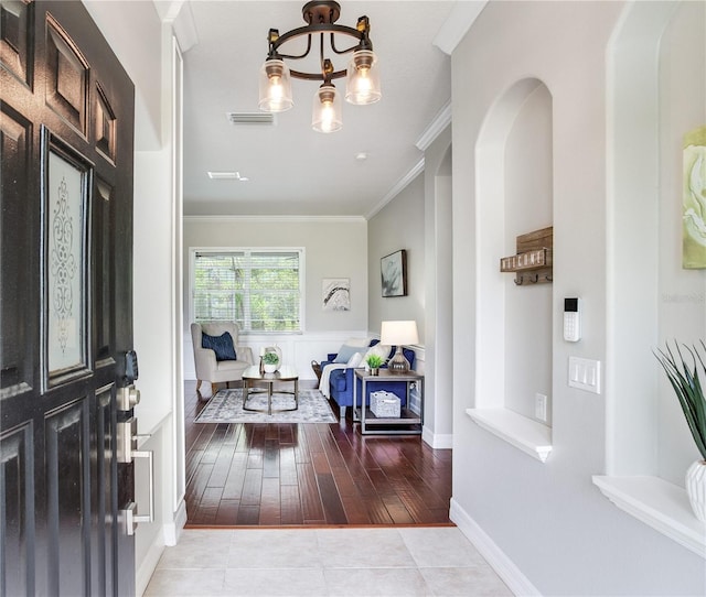 tiled foyer featuring ornamental molding, a chandelier, and baseboards