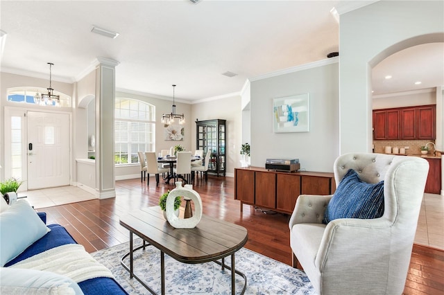 living room featuring arched walkways, a chandelier, hardwood / wood-style floors, crown molding, and baseboards