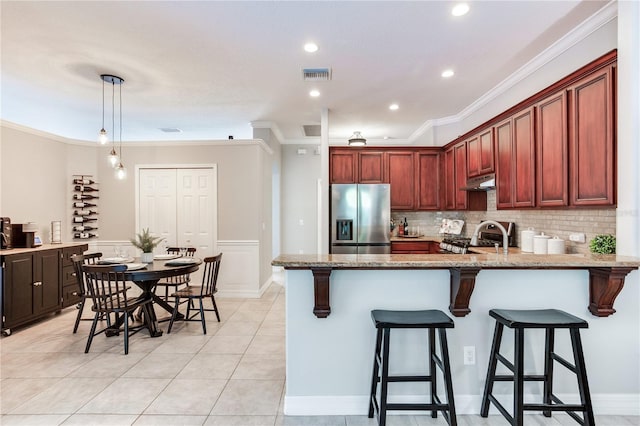 kitchen featuring stainless steel refrigerator with ice dispenser, under cabinet range hood, a peninsula, ornamental molding, and light stone countertops