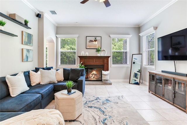 living area featuring ceiling fan, plenty of natural light, a glass covered fireplace, ornamental molding, and light tile patterned floors