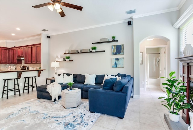 living room featuring arched walkways, light tile patterned floors, crown molding, ceiling fan, and baseboards