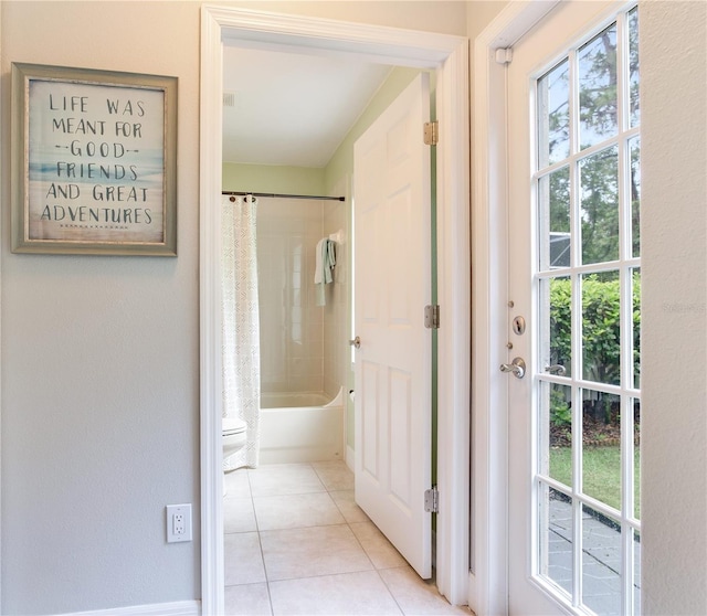 full bathroom with tile patterned floors, healthy amount of natural light, shower / bathtub combination with curtain, and toilet