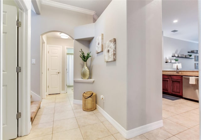 hall featuring crown molding, arched walkways, light tile patterned flooring, baseboards, and a sink