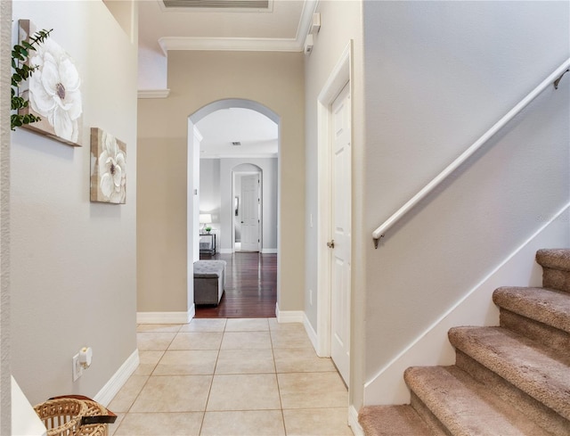 corridor featuring arched walkways, crown molding, stairs, light tile patterned flooring, and baseboards