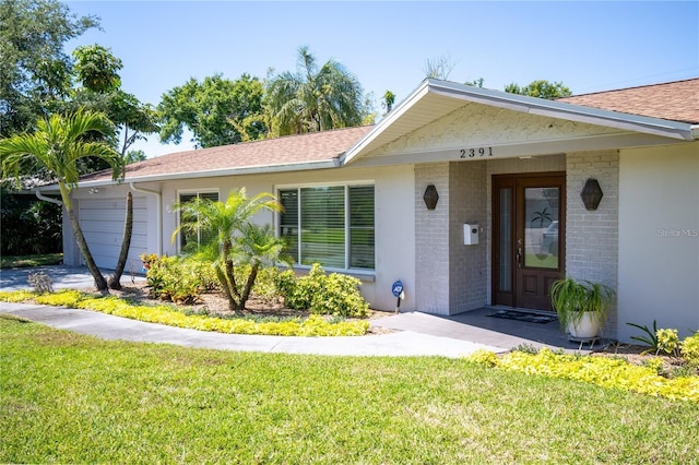 ranch-style home with an attached garage, brick siding, a shingled roof, and a front yard