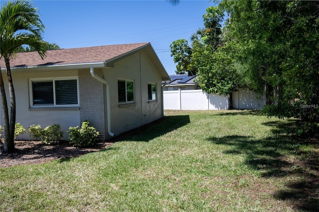 view of property exterior with roof with shingles, fence, a lawn, and brick siding