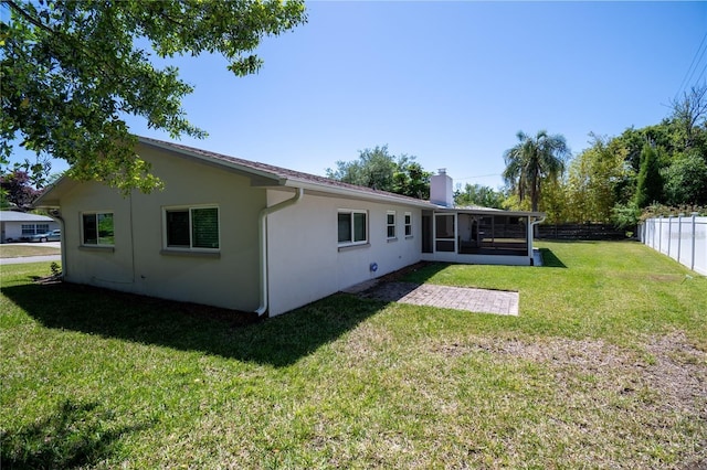 back of property with fence, a sunroom, a yard, stucco siding, and a chimney