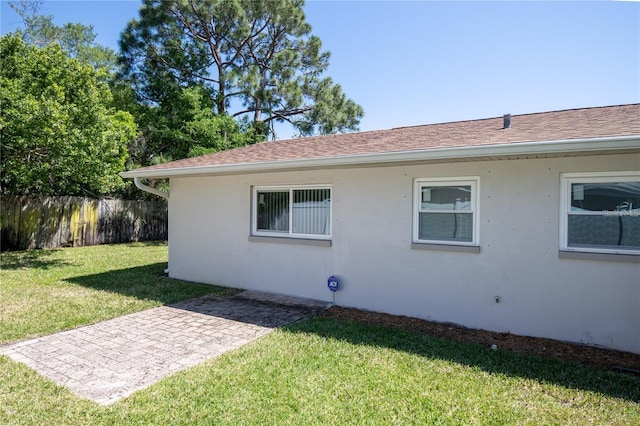 view of home's exterior featuring a yard, a shingled roof, fence, and stucco siding