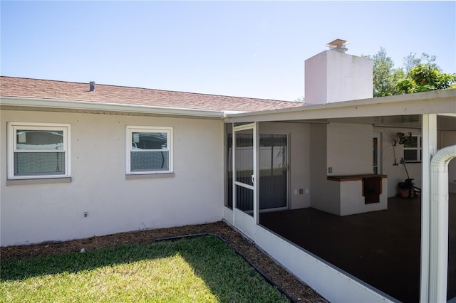 back of property featuring roof with shingles, a chimney, a lawn, and stucco siding