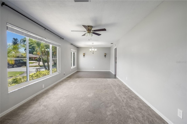 empty room featuring baseboards, dark carpet, a textured ceiling, and ceiling fan with notable chandelier