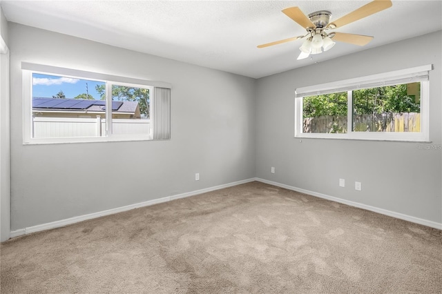 empty room with light carpet, ceiling fan, baseboards, and a textured ceiling