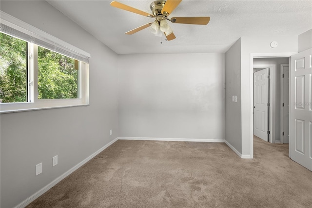 unfurnished room featuring ceiling fan, baseboards, a textured ceiling, and light colored carpet