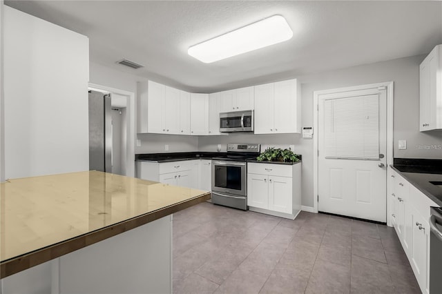 kitchen featuring stainless steel appliances, dark countertops, white cabinets, and visible vents