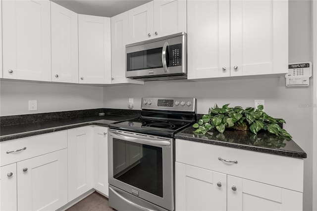 kitchen featuring appliances with stainless steel finishes, dark stone countertops, and white cabinets