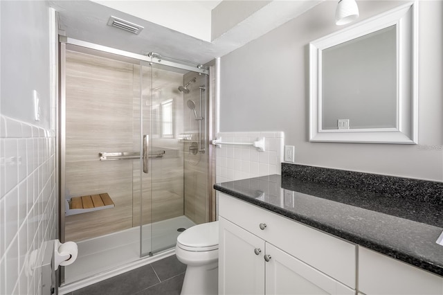 bathroom featuring toilet, tile walls, visible vents, tile patterned floors, and a stall shower