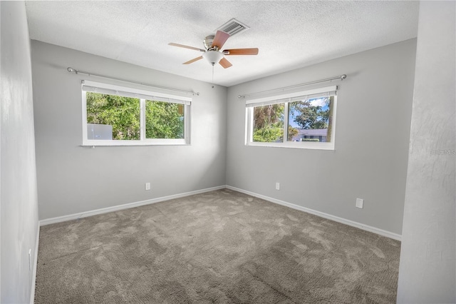 unfurnished room with a textured ceiling, carpet flooring, visible vents, and baseboards