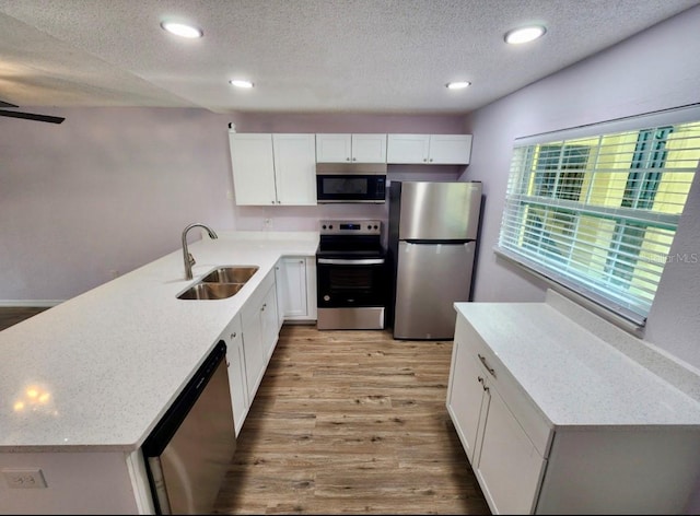 kitchen featuring sink, appliances with stainless steel finishes, a textured ceiling, white cabinets, and light wood-type flooring