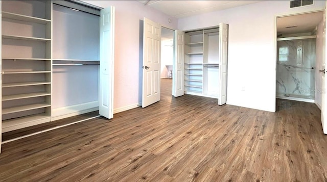 unfurnished bedroom with wood-type flooring and two closets