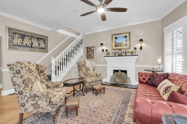 living room with stairway, a fireplace with raised hearth, crown molding, and wood finished floors