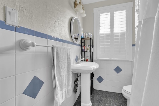 full bathroom featuring tile walls, a textured wall, toilet, wainscoting, and speckled floor