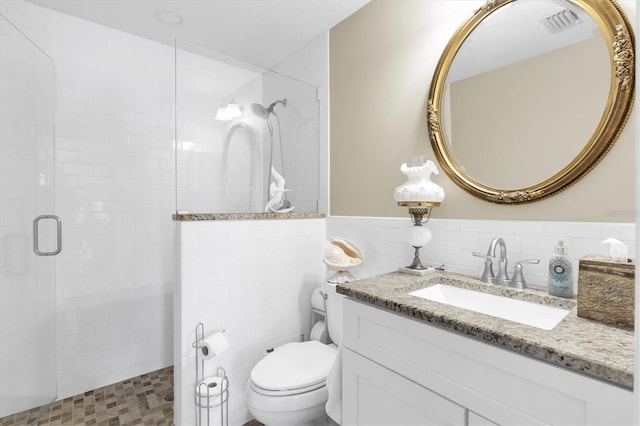 bathroom with tile walls, visible vents, toilet, a shower stall, and vanity