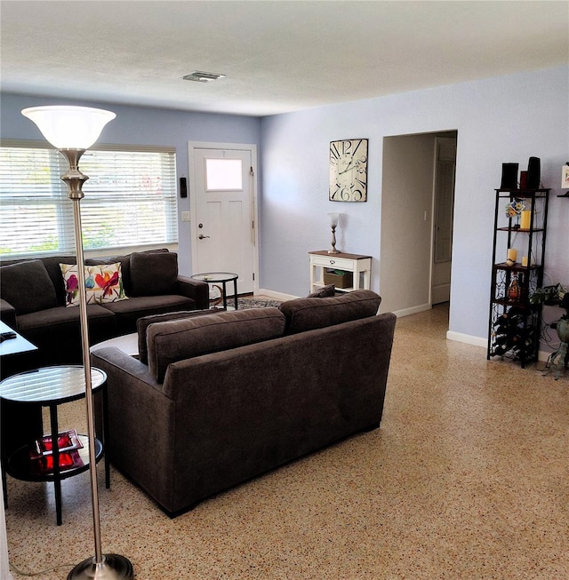 living area with a wealth of natural light, visible vents, light speckled floor, and baseboards