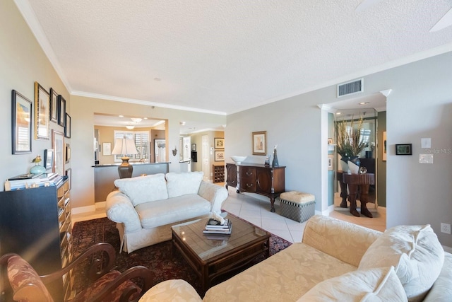 living area featuring visible vents, ornamental molding, light tile patterned flooring, a textured ceiling, and baseboards