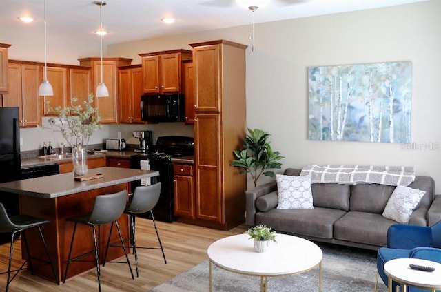 kitchen featuring a kitchen island, decorative light fixtures, a kitchen bar, black appliances, and light wood-type flooring