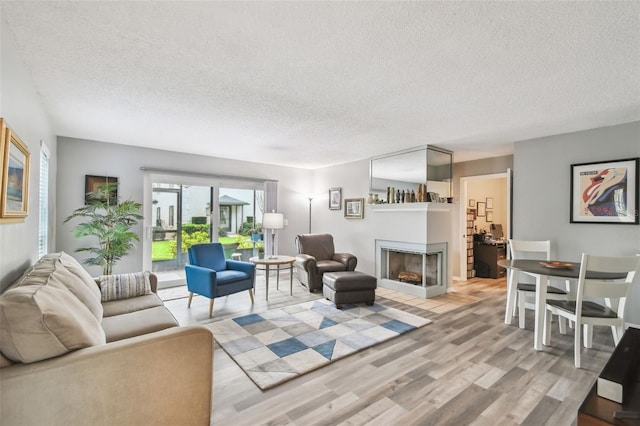 living room featuring a multi sided fireplace, light hardwood / wood-style floors, and a textured ceiling